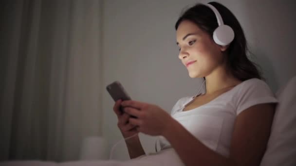 Kvinna med smartphone och hörlurar i sängen — Stockvideo