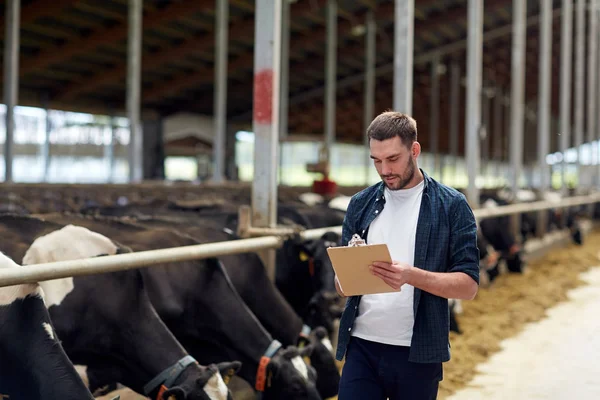 Agricultor con portapapeles y vacas en establo en la granja —  Fotos de Stock