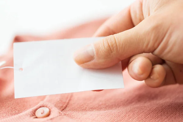 Close up of hand with price tag and clothing item — Stock Photo, Image