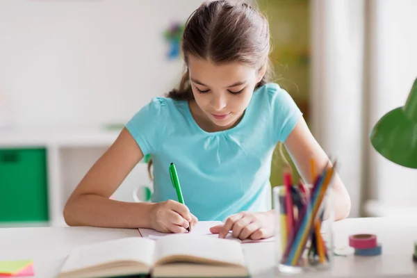 Menina feliz com livro escrevendo para notebook em casa — Fotografia de Stock