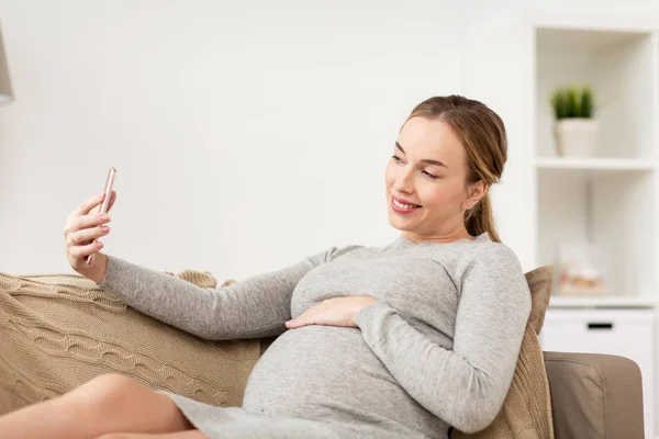 Беременная женщина делает селфи на смартфоне дома — стоковое фото