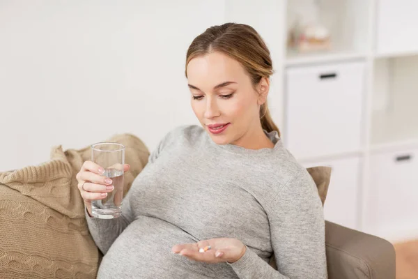 Gelukkig zwangere vrouw met water en pillen thuis — Stockfoto