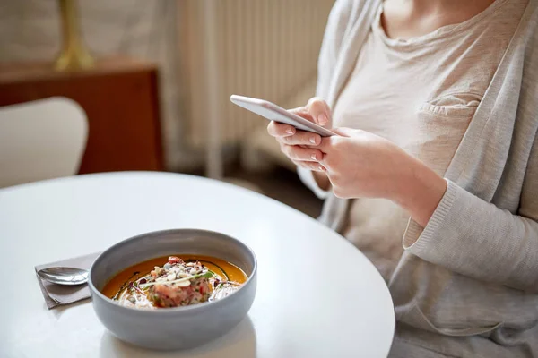 Женщина со смартфоном и тыквенным супом в кафе — стоковое фото