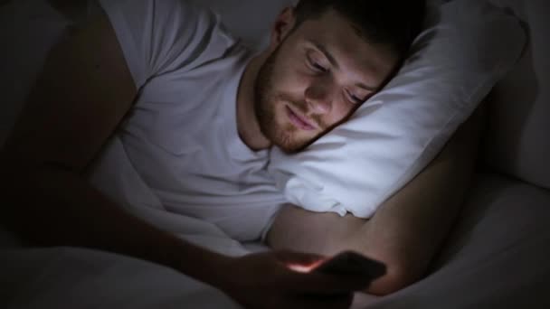 Jovem com smartphone na cama à noite — Vídeo de Stock