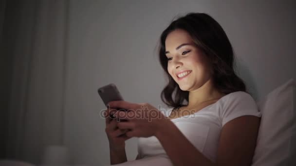 幸福的年轻女人，与智能手机在床上 — 图库视频影像