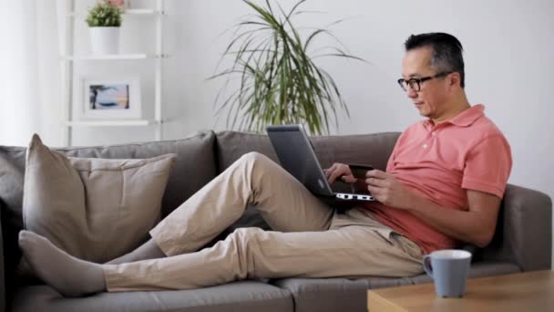 ノート パソコンと自宅のソファの上のクレジット カードを持つ男 — ストック動画