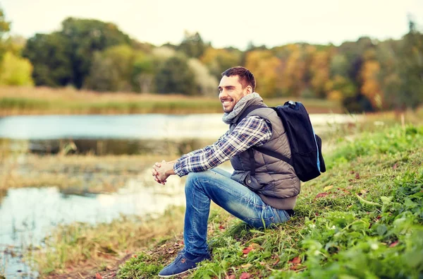 Sonriente hombre con mochila descansando en la orilla del río —  Fotos de Stock