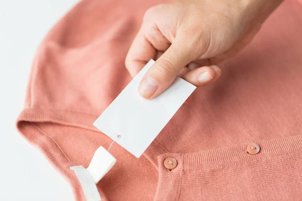 Close up of hand with price tag and clothing item — Stock Photo, Image