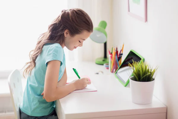 Chica con la escritura de la PC tableta a la libreta en casa —  Fotos de Stock