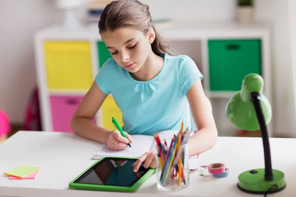 Κορίτσι με tablet pc γράφοντας στο σημειωματάριο στο σπίτι — Φωτογραφία Αρχείου