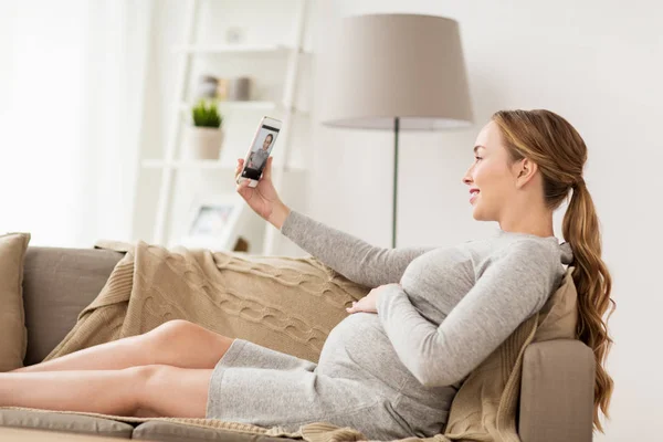 Беременная женщина делает селфи на смартфоне дома — стоковое фото