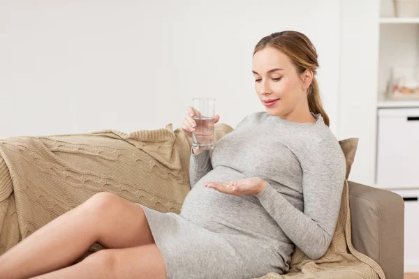 Glückliche Schwangere mit Wasser und Pillen zu Hause — Stockfoto
