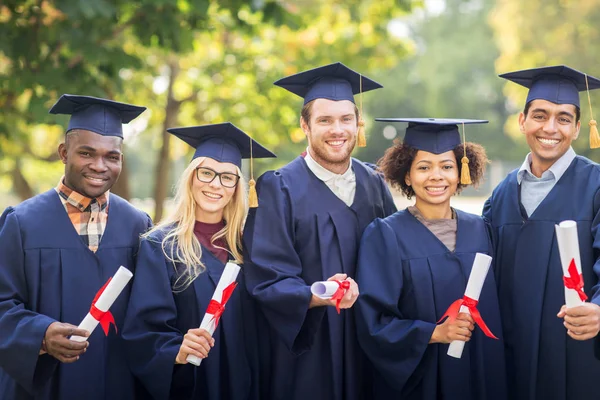 Šťastní studenti v minometných tabulích s diplomy — Stock fotografie
