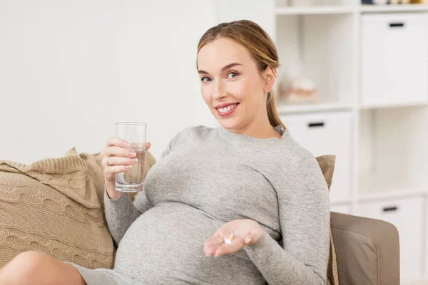 Glückliche Schwangere mit Wasser und Pillen zu Hause — Stockfoto