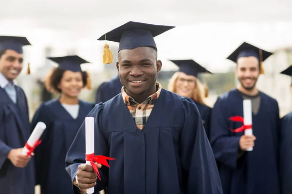 Glada studenter i murbruk styrelser med diplom — Stockfoto