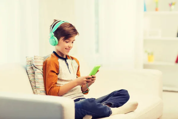 Niño feliz con teléfono inteligente y auriculares en casa —  Fotos de Stock