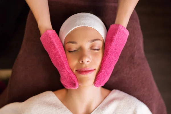 Femme ayant massage du visage avec des gants éponge au spa Photo De Stock