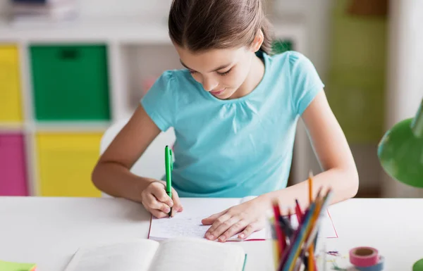 Menina feliz com livro escrevendo para notebook em casa — Fotografia de Stock