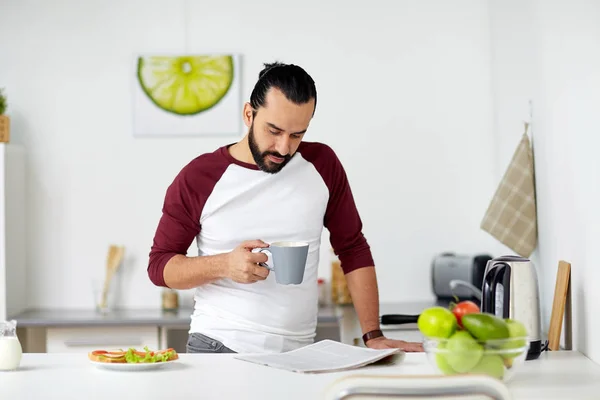 Hombre leyendo periódico y comiendo en casa cocina —  Fotos de Stock