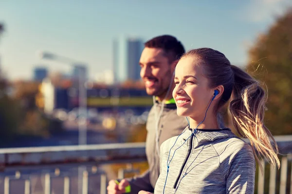 Feliz pareja con auriculares funcionando en la ciudad — Foto de Stock