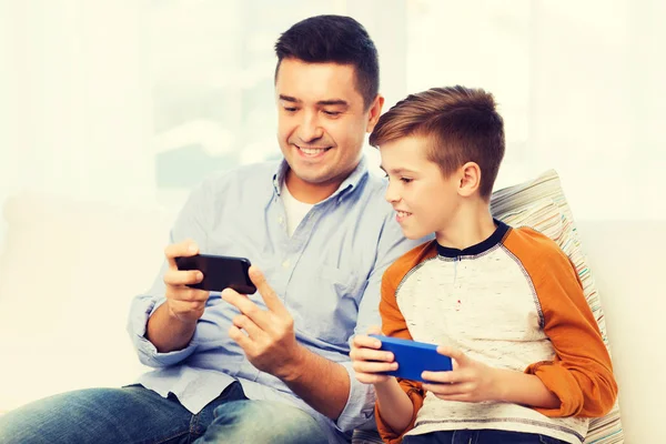 Счастливый отец и сын со смартфонами дома — стоковое фото