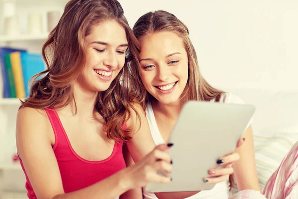 Счастливые друзья или девочки-подростки с планшетным компьютером дома — стоковое фото