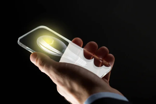 Närbild på hand med glödlampa på smartphone — Stockfoto