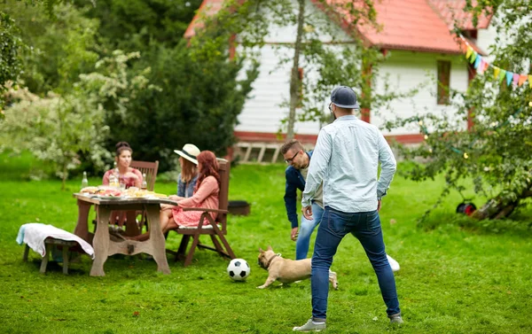 Amigos jugando al fútbol con perro en el jardín de verano —  Fotos de Stock