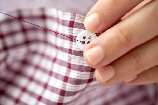 Mujer con puntadas de aguja en el botón a la camisa — Foto de Stock