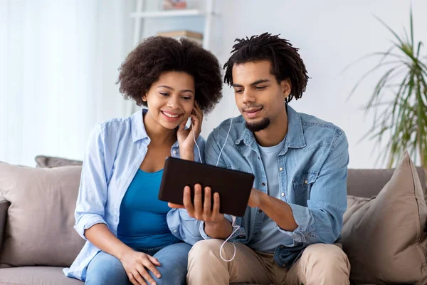 Feliz pareja con tablet PC y auriculares en casa —  Fotos de Stock