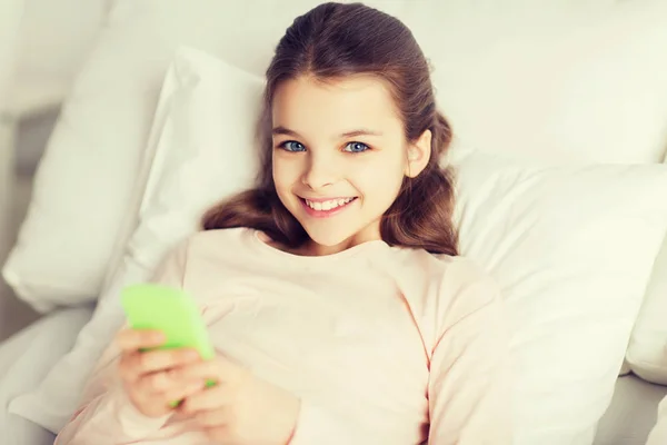 Chica feliz acostada en la cama con teléfono inteligente en casa —  Fotos de Stock