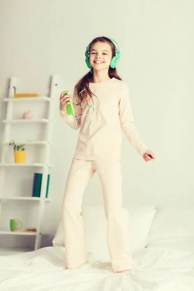 Дівчина стрибає на ліжку зі смартфоном та навушниками — стокове фото