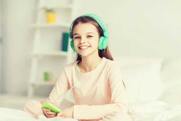 Κορίτσι που κάθεται στο κρεβάτι με το smartphone και ακουστικά — Φωτογραφία Αρχείου