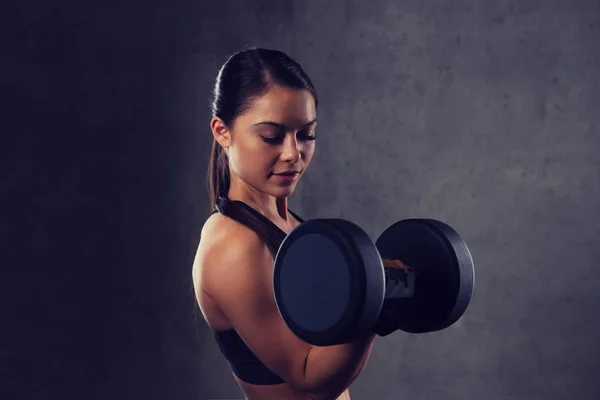 Mujer joven flexionando los músculos con pesas en el gimnasio —  Fotos de Stock