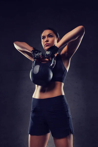 Mujer joven flexionando los músculos con kettlebell en el gimnasio —  Fotos de Stock