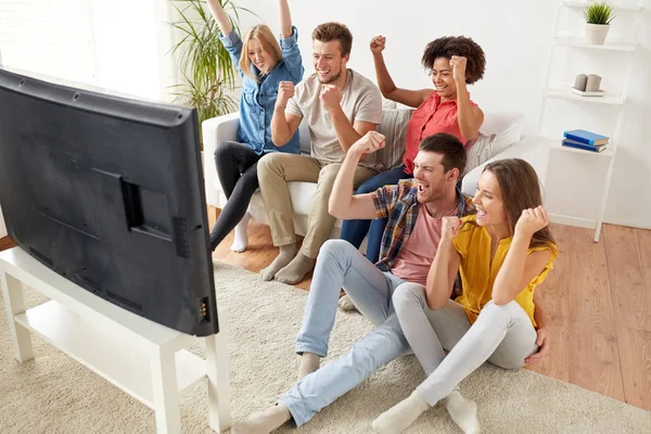 Amigos felizes com controle remoto assistindo tv em casa — Fotografia de Stock