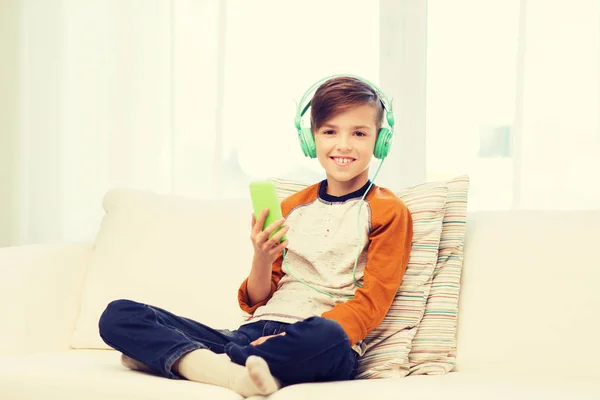 Szczęśliwy chłopiec ze smartfonem i słuchawkami w domu — Zdjęcie stockowe