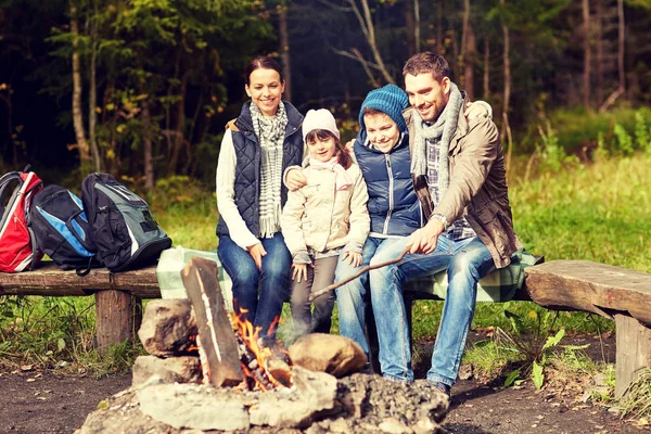 Familia feliz sentado en el banco en el fuego del campamento —  Fotos de Stock