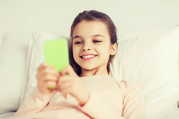 Счастливая девушка лежит в постели со смартфоном дома — стоковое фото