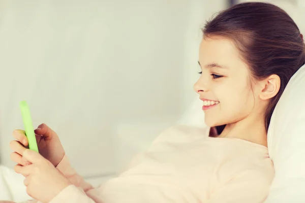 Chica feliz acostada en la cama con teléfono inteligente en casa —  Fotos de Stock