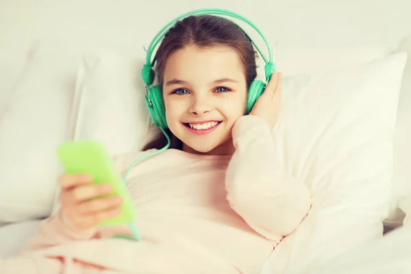 Menina feliz deitado na cama com smartphone em casa — Fotografia de Stock