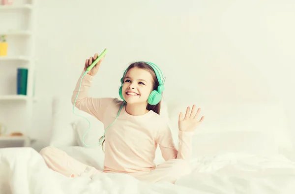 Mädchen sitzt mit Smartphone und Kopfhörer im Bett — Stockfoto