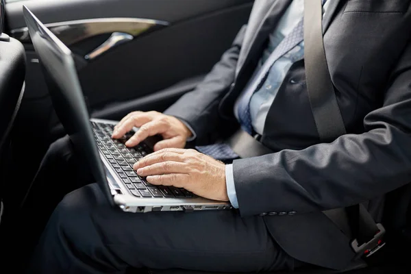Senior businessman with laptop driving in car — Stock Photo, Image