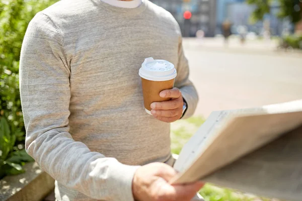 senior man with coffee reading newspaper outdoors