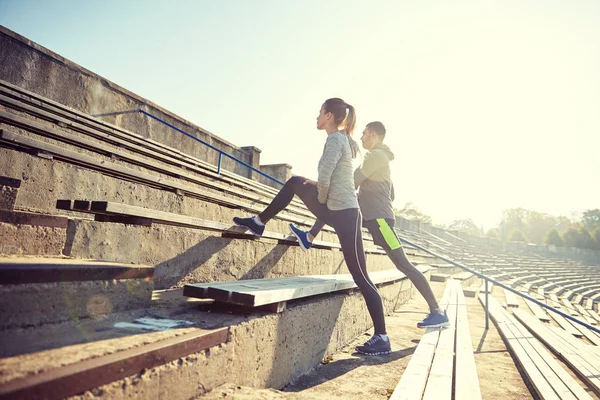 Couple stretching leg on stands of stadium — Stock Photo, Image