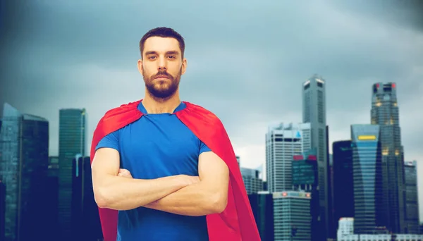Mężczyzna w czerwonym superhero cape na tle miasta — Zdjęcie stockowe