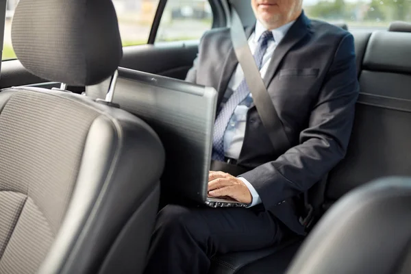 Senior Geschäftsmann mit Laptop im Auto unterwegs Stockbild