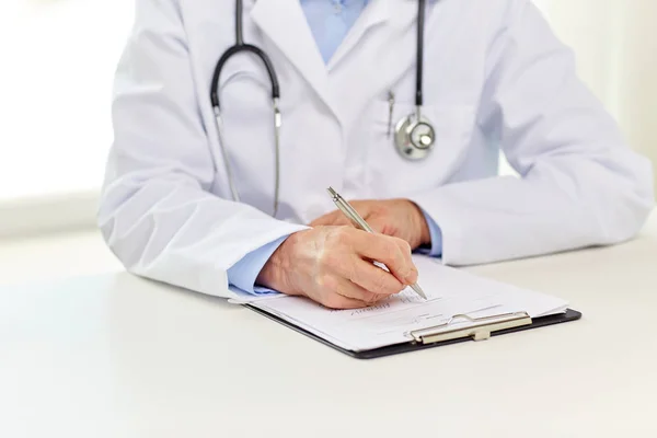 Senior doctor with clipboard writing at hospital — Stock Photo, Image