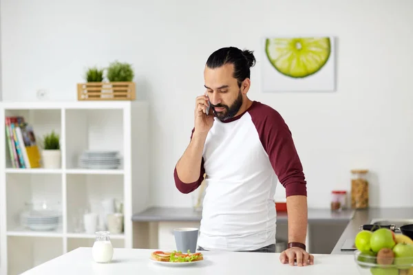 Człowieka, wywołując na smartfonie i jedzenie w domu — Zdjęcie stockowe