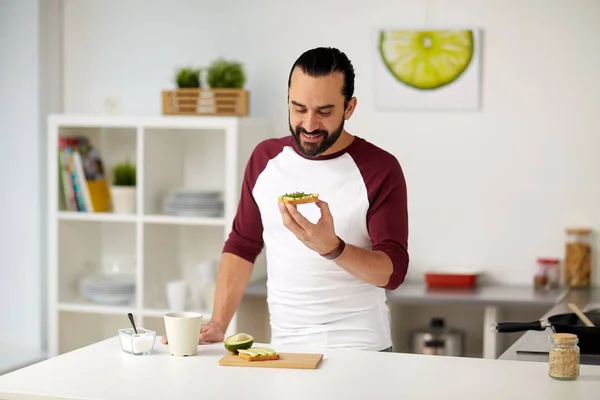 Hombre comiendo bocadillos de aguacate en casa cocina —  Fotos de Stock